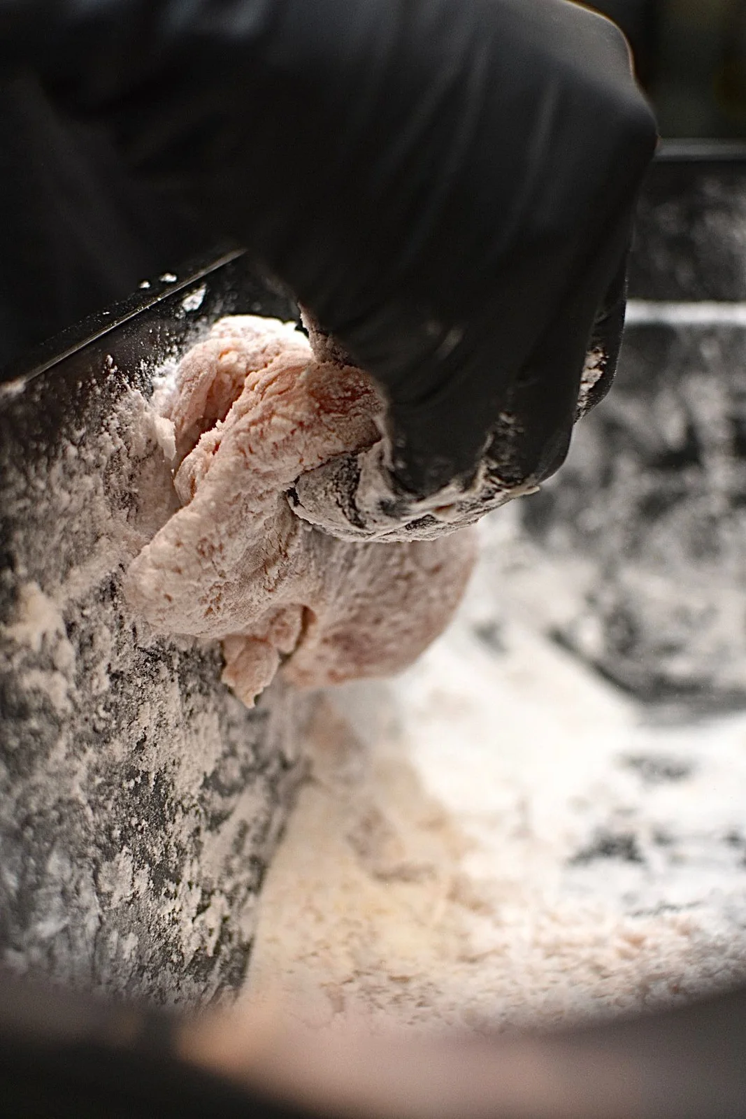 A gloved hand shaping fresh ramen dough in flour